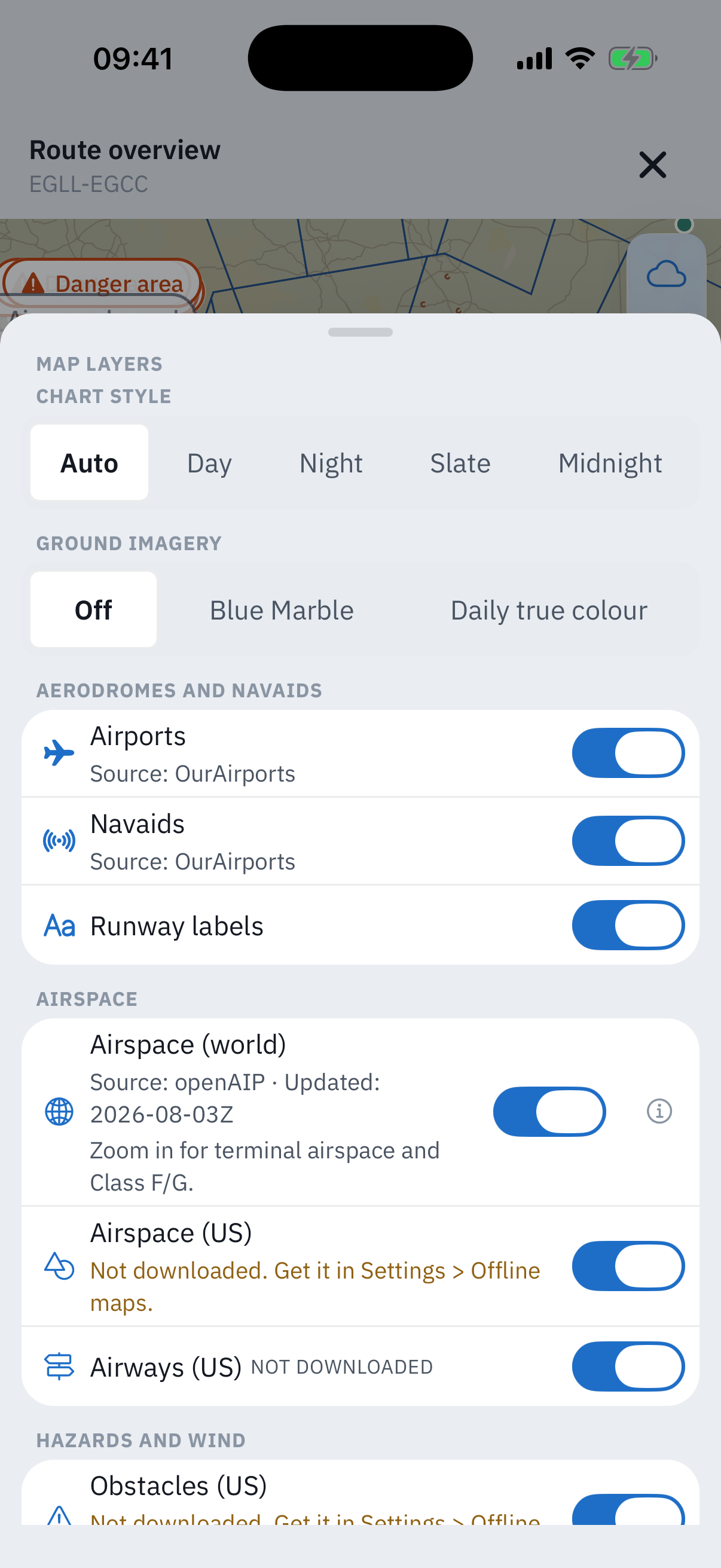 The Map layers sheet over the route chart: a Chart style control with Auto, Day, Night, Slate and Midnight, a Ground imagery control set to Off with Blue Marble and Daily true colour options, then rows for Airports and Navaids each credited Source: OurAirports, Runway labels, Airspace world credited Source: openAIP updated 2026-08-03Z with a zoom-in note, and Airspace US with the amber line Not downloaded, get it in Settings, Offline maps